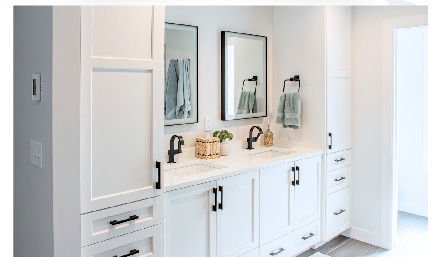 Custom white double vanity with black hardware, framed mirrors, and tall linen towers in a primary bathroom remodel by Elias Construction in Rochester, MN