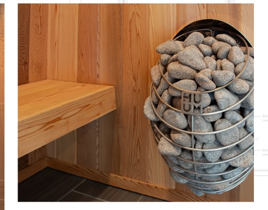 Stainless sauna heater filled with stones next to a cedar bench in a custom home sauna